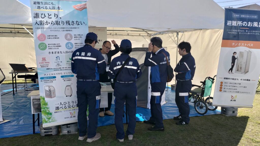 内閣府（防災担当）の方々がブースでナノミストバスの説明を聞く様子